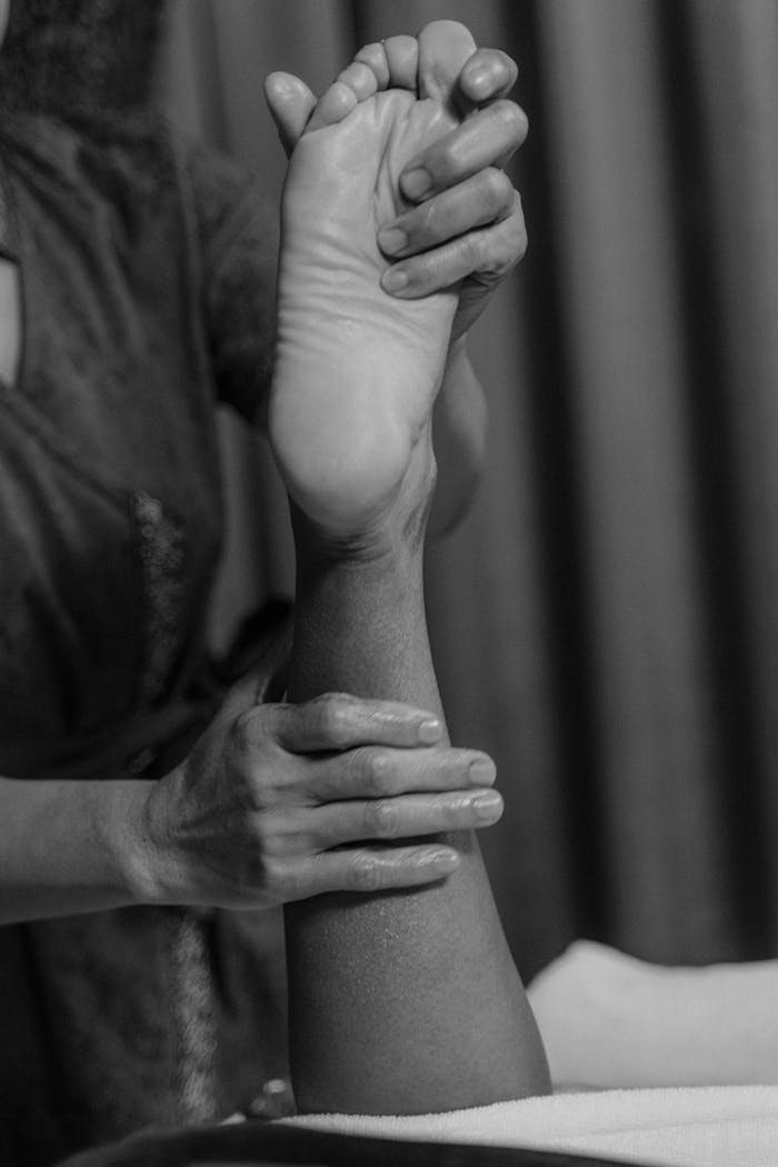 A black-and-white image of a massage therapist performing an ankle and foot massage.